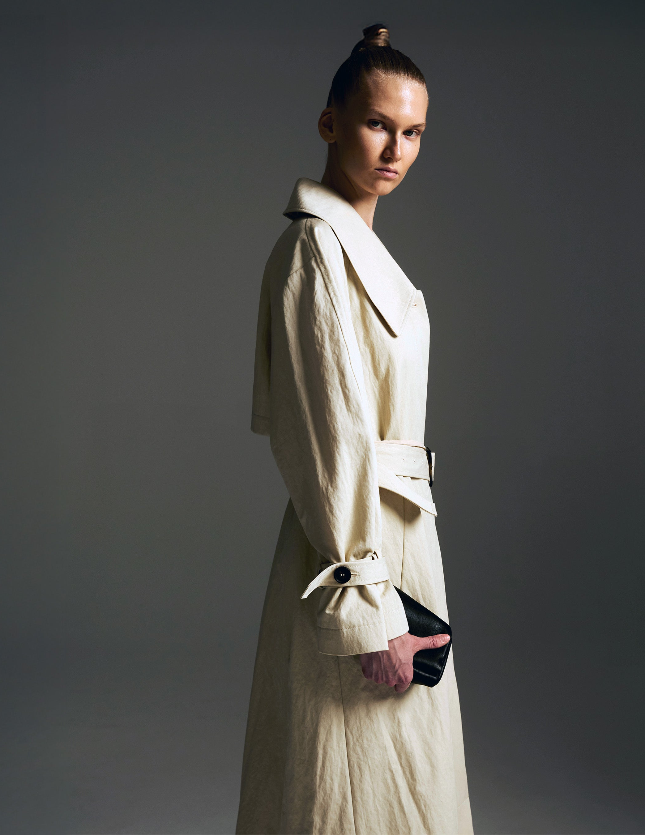 Model wearing a white trench coat against a gray background