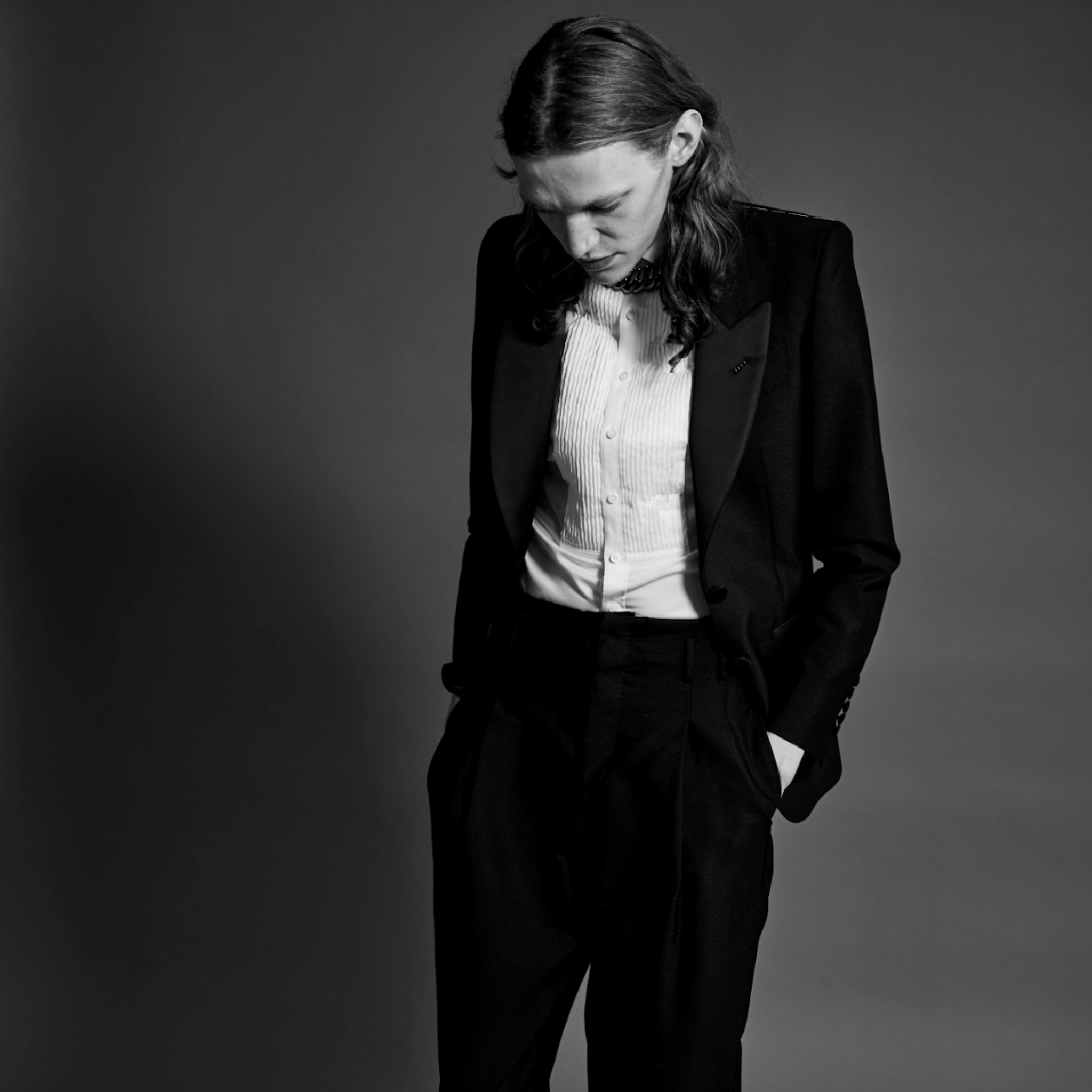 Person wearing a black suit and white shirt against a gray background